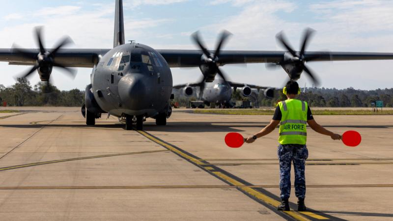An aircraft is guided by a man in military uniform and hi-vis. 