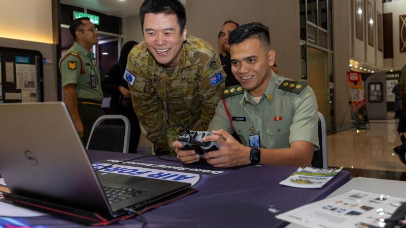 Two men in military uniform play on a laptop.