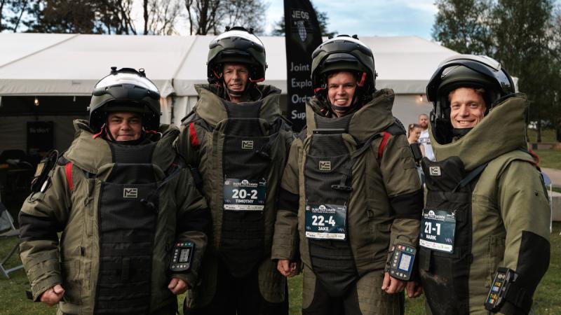 Four men wearing bomb suits standing outside a marquee. 