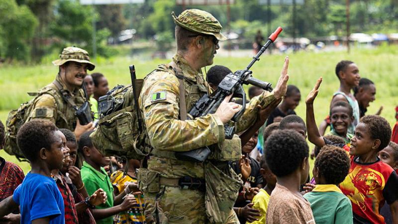 An Australian soldier walks with a group of PNG children around him.