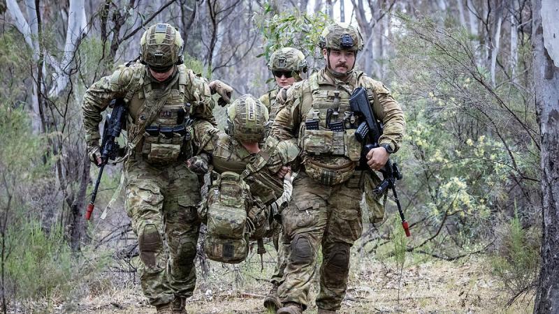 Soldiers in the bush carry a person who is posing as a casualty.
