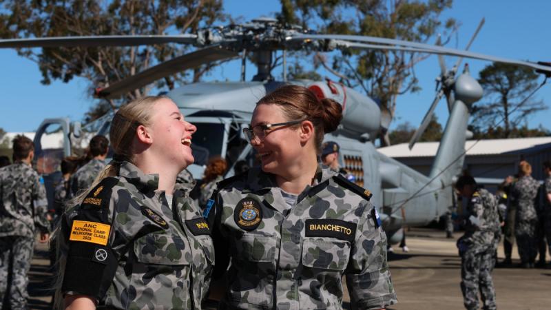 Two Australian Navy Cadets enjoy a laugh at the ANC national camp, with a helicopter in the background.