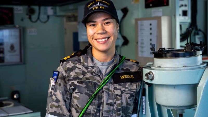 A sailor in uniform standing on the bridge of a frigate.