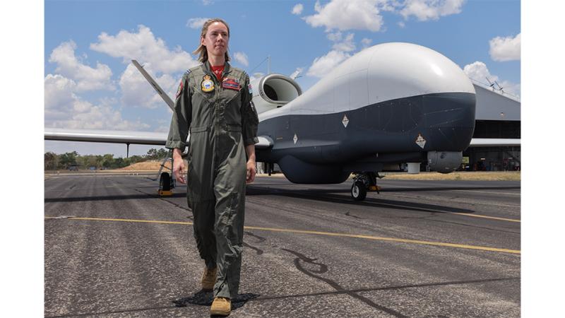 A woman in military uniform standing before an aircraft.