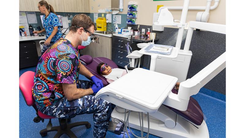 A dentist and assistant examine a young girl in a dental office.