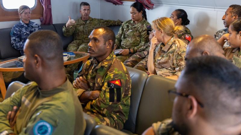 A group of military personnel sitting in a discussion group on board a ship.