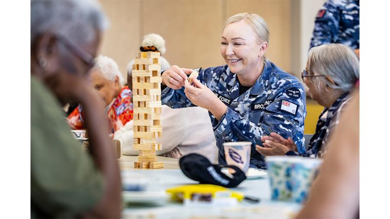 A military member plays Jenga with elderly civilians.