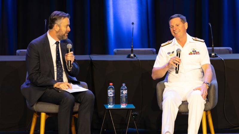 Two men sitting in chairs in a stage talking to each other using microphones. One Navy, one civilian.