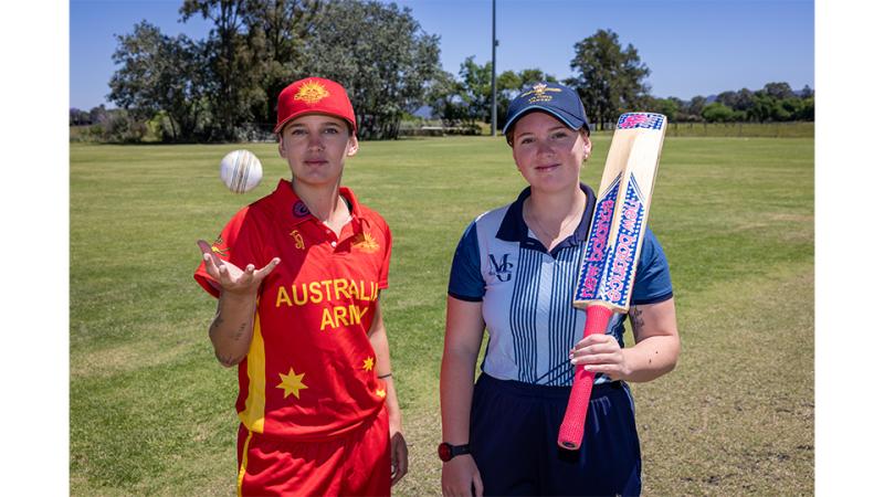 Two girls in athleisure stand on a field, one with a baseball and the other with a bat.
