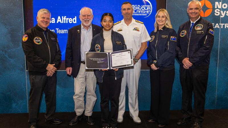 Six people pose for a photo, with a student in the centre holding an Endeavour Scholarship certificate.