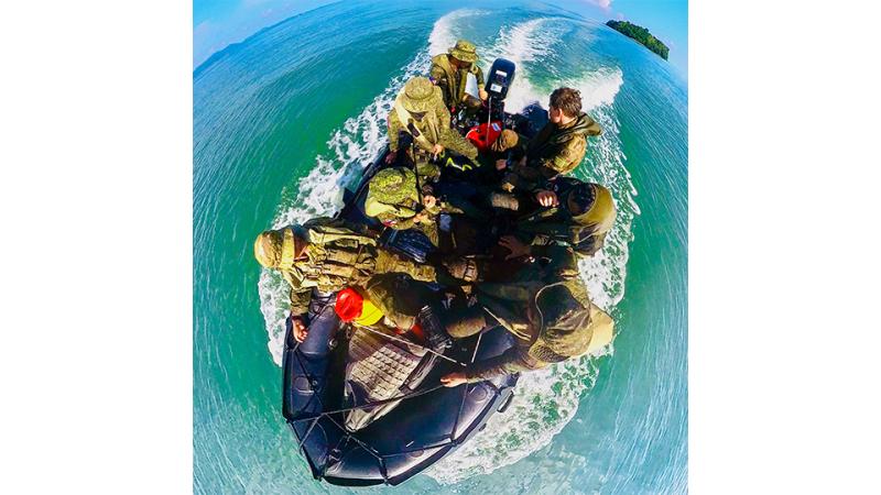 Military personnel with life vests in a black boat.