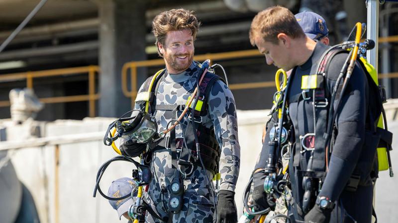 Two navy personnel in diving gear, one from Australia and one form the US, stand talking.