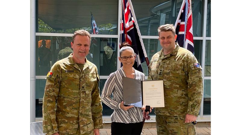 Two male military personnel and a female civilian with an award.