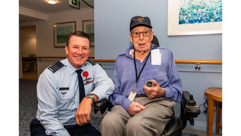 A man in military uniform beside an elderly man in a wheelchair.