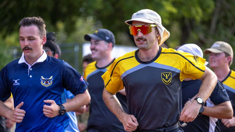 An Army signaller in civilian clothing and sunglasses runs with others.