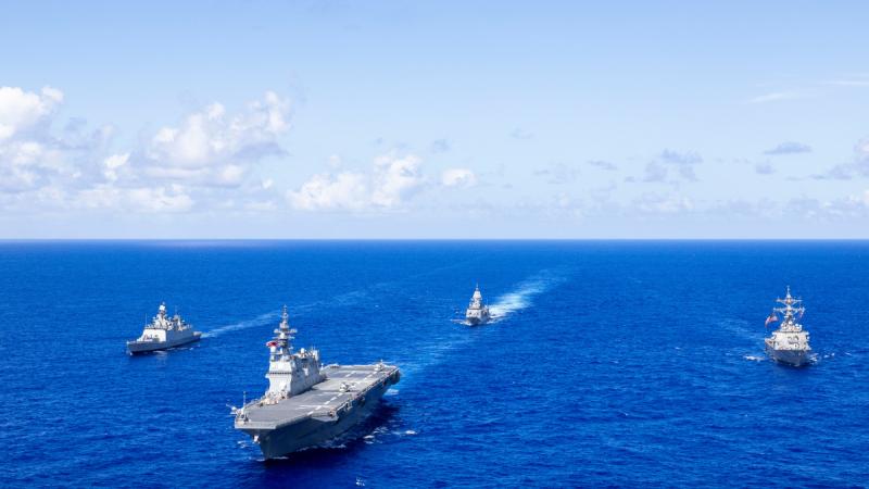 Four naval ships sail in formation in the open ocean.