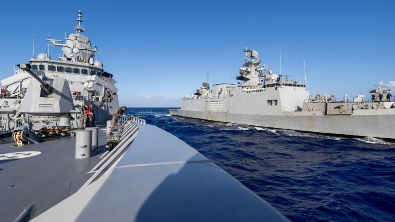 Two frigates side by side in the ocean, connected by a thin yellow rope.