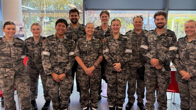 A group of 10 Navy crew members in uniform smiling together inside a building.