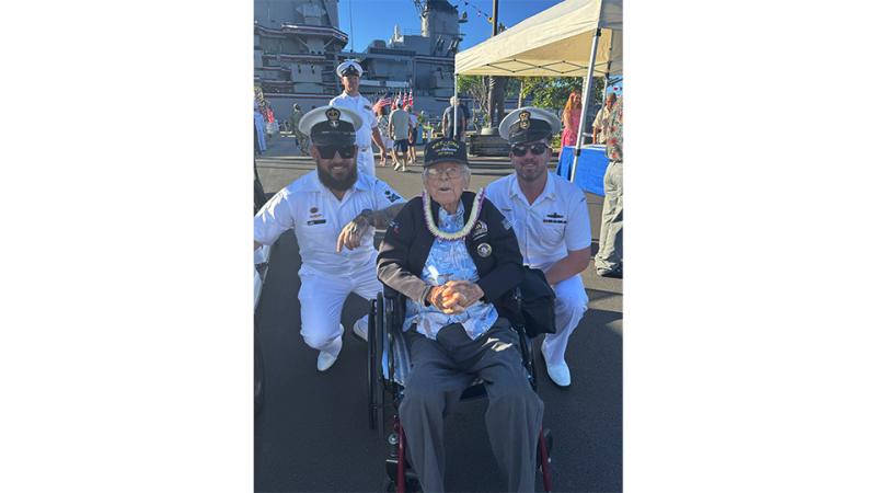 Two Royal Australian Navy sailors crouch beside an elderly man in a wheelchair, with USS Missouri visible in the background.