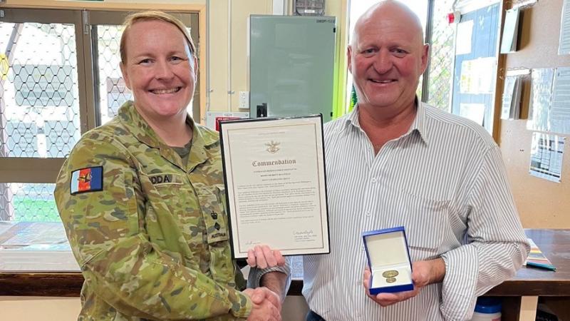 A military officer presents a commendation certificate and medallion to a civilian.