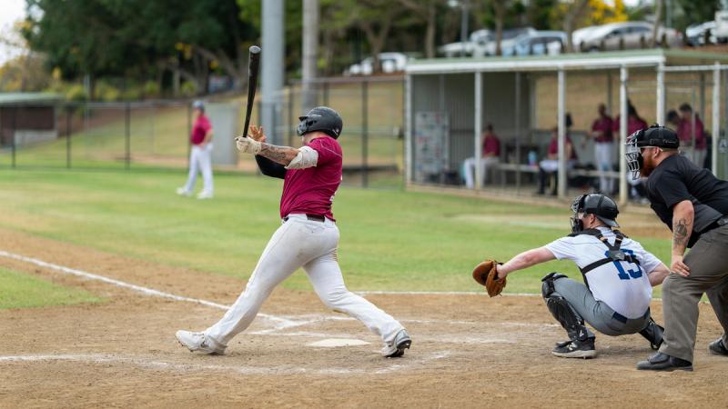 A baseball batter in a maroon shirt follows through after swinging during a game at the ADF National Baseball Championships.