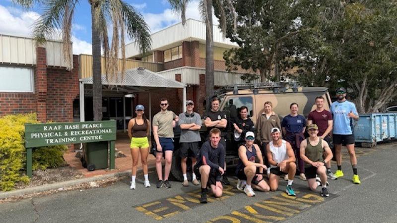 Thirteen aviators in sports gear stand outside the Physical and Recreational Training Centre at RAAF Base Pearce, posing for a group photo.