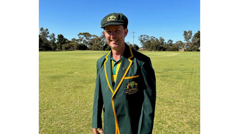 A man in a green and gold cricket uniform with blazer. 