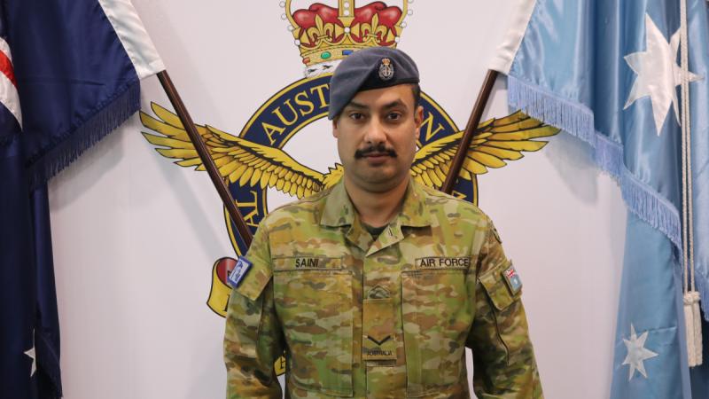 Leading Aircraftman Jagdeep Saini stands before Australian and Air Force flags.
