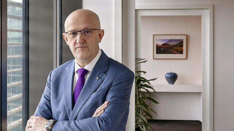 Mike Burgess standing with his arms crossed beside a window in an office.