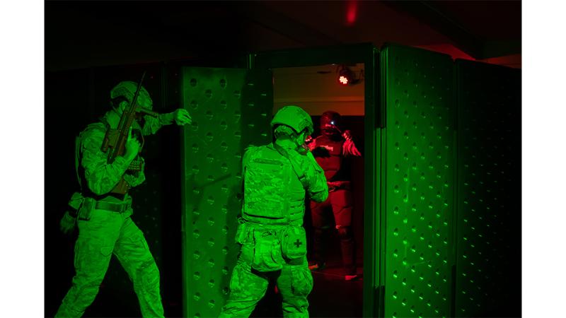 Three men in military uniform train in the dark.