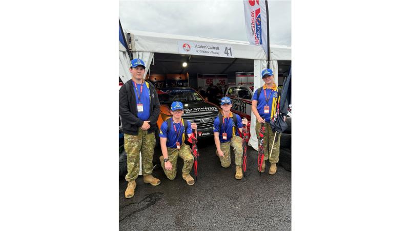 Youth in military uniform stand before a tent and car.