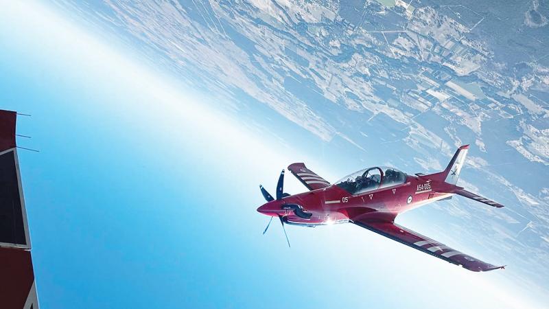 An aircraft flies upside down with earth and sky in the background.