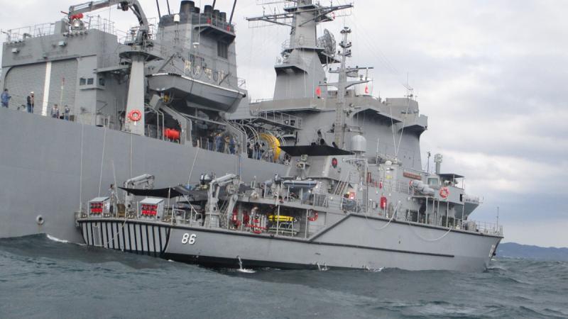 A medium-sized ship pulls up next to a large ship on the water.