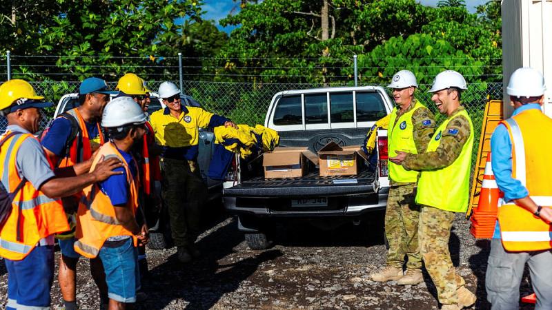 A group of Fijian builders and Australian Army soldiers gather around a ute filled with building materials.