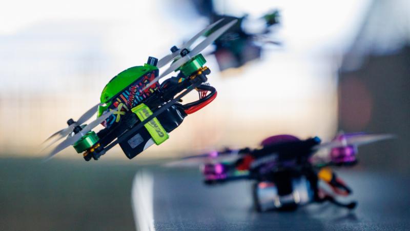 A green drone hovers at an angle above a table.
