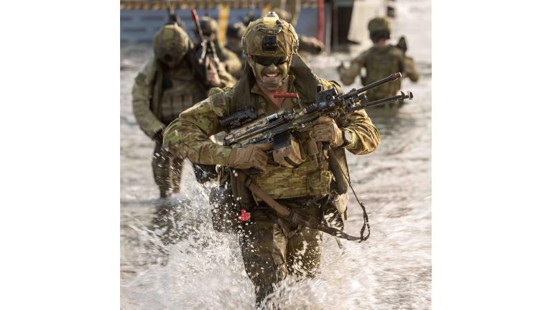 A soldier holding a gun runs through water with others following.