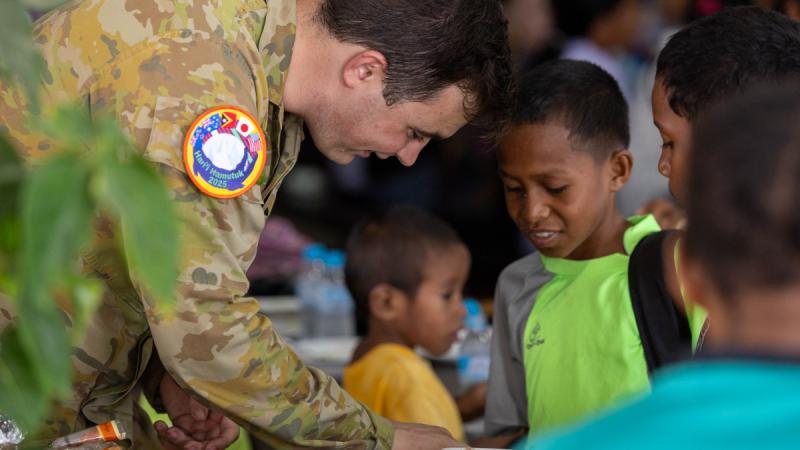 A man in uniform places food on a plate held by a boy.
