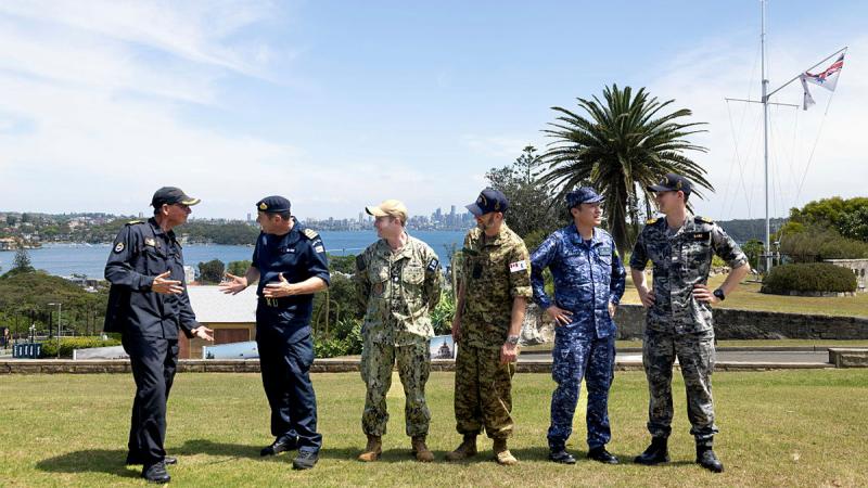 Defence personnel in uniform chat casually on a fine day with a palm tree in the background.