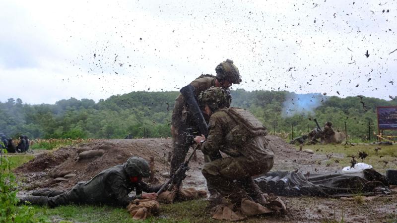 Three soldiers amid flying dirt and debris, with one crouching, another lying down and the third standing.