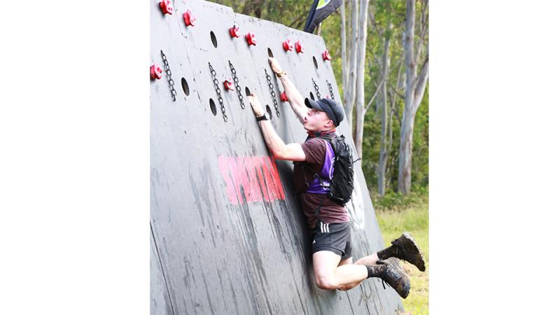 A man moves across an angled wall with holes, climbing holds and short chains.