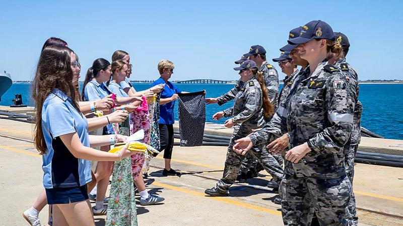 A line of students faces a line of Navy personnel holding out laundry bag gifts.
