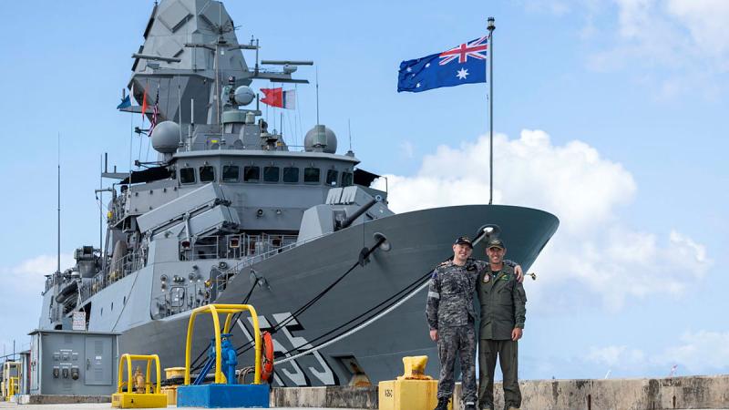 Two men - a father and his adult son - stand in front of a Navy ship tied up at a wharf.
