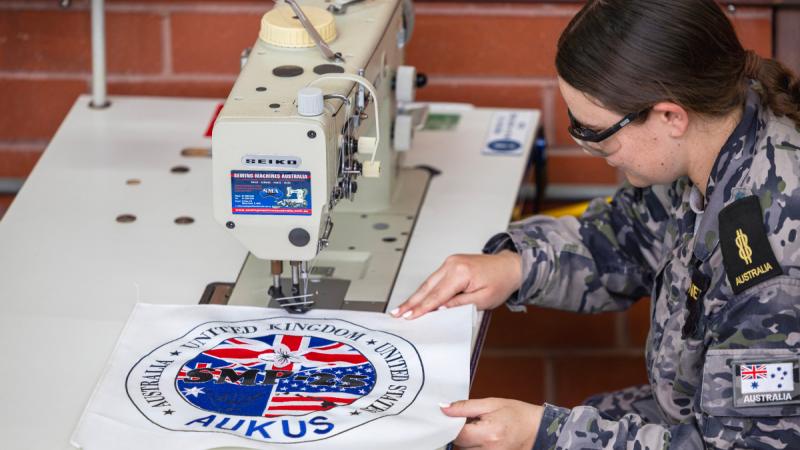 A sailor stitches the AUKUS logo using a sewing machine.