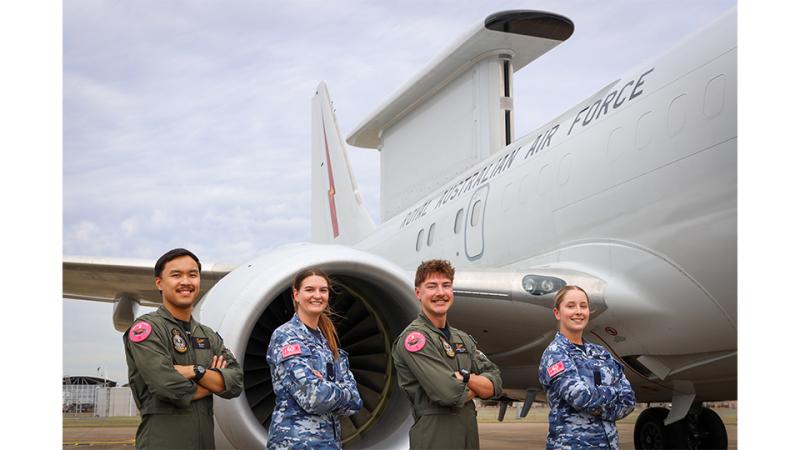 Four military personnel wearing a pink shoulder patch stand before an aircraft. 