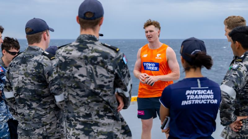 A GWS Giants players in orange talks with Navy sailors onboard ship at sea..