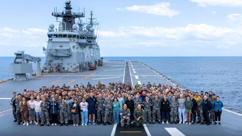 HMAS Canberra crew are joined by families and guests on the flight deck for a whole ship photo off the NSW coast.