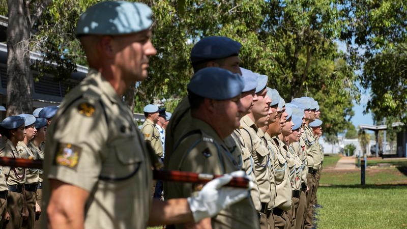 Army personnel in uniform stand in lines with blue berets on.