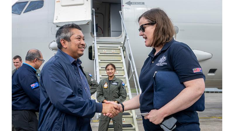 A man and woman shake hands before an aircraft.