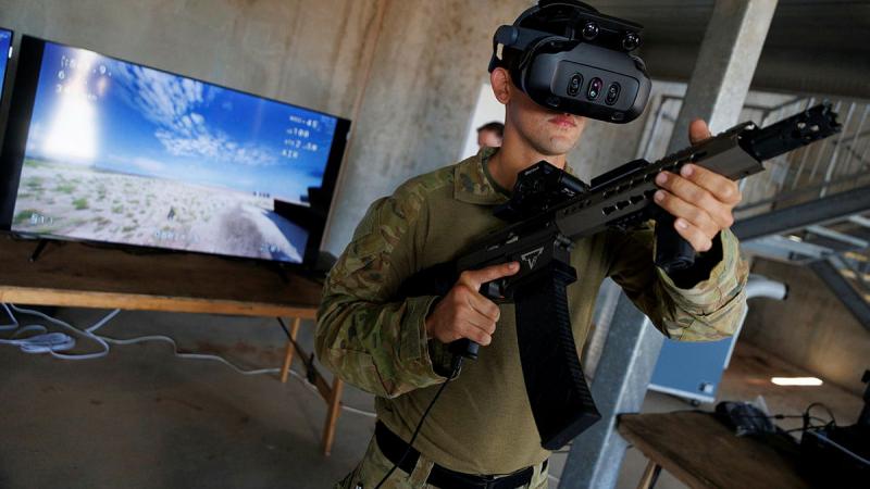 Am Army member holds a weapon and wear goggles as he faces away from a simulation screen.