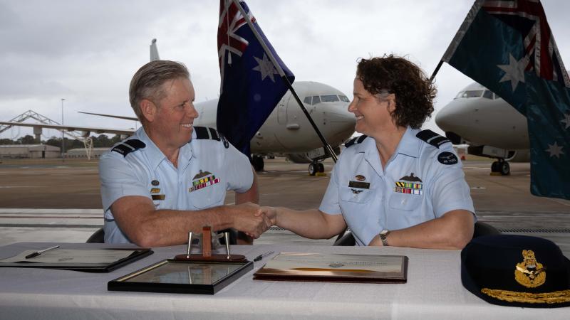 A man and woman in military uniform shake hands before Australian flags and aircraft.